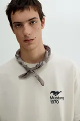 Remera color crema de corte holgado con estampado de un caballo Mustang y el año 1970 en el pecho. Cuello redondo con ribete fino y hombros caídos.