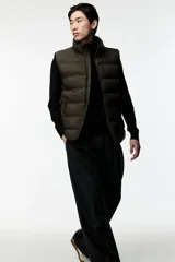 Chaleco puffer color verde oliva, con cuello alto y cierre frontal. Cuenta con bolsillos laterales con cierre y un bolsillo interno con botón a presión.