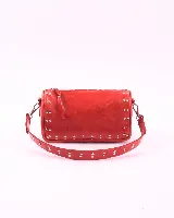 Bandolera roja de cuero con tachas plateadas, cierre superior con cremallera y correa de cuero desmontable con tachas.