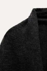 Capa tipo chal color gris oscuro confeccionada en tejido de punto con lana y alpaca. Tiene cuello alto y terminación con flecos.