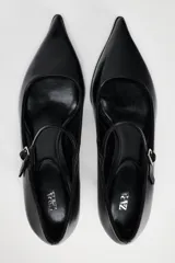 Zapato de cuero negro con tacón kitten, tira delantera con hebilla ajustable y punta fina.