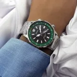 Reloj Casio plateado con esfera negra, bisel verde con indicadores de puntos cardinales, agujas luminiscentes, calendario y brazalete de acero inoxidable.