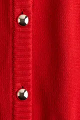 Cárdigan rojo de punto con cuello redondo, manga corta, cierre frontal con botones metálicos y bolsillos delanteros.