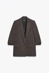 Blazer color marrón oscuro, abierta, con cuello solapa y hombreras. Manga tres cuartos con trabilla y botón dorado. Bolsillos delanteros con solapa.