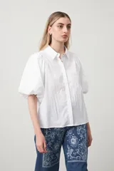 Camisa blanca de algodón con cuello camisero y mangas cortas abullonadas. Presenta un corte relajado y cierre frontal de botones.