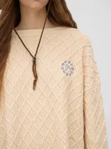 Sweater color crema con tejido en ochos, cuello redondo, puños acanalados con doble raya azul y tajos a los costados.