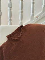 Buzo color marrón con cuello alto y mangas largas terminadas en volados.