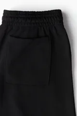 Pantalón de jogging negro de corte ancho y tiro alto, confeccionado en tejido de felpa con interior cepillado suave. Presenta cintura elástica fruncida con cordón oculto, bolsillos laterales discretos y un bolsillo trasero abierto.