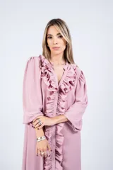 Vestido largo color crudo, estilo camisero, con cuello en V y volados verticales en el frente. Tiene mangas largas abullonadas y corte amplio.