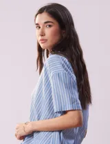 Blusa celeste y blanca a rayas verticales, con cuello con solapa y escote en V. Delantera cruzada con abertura simulada y mangas cortas.