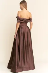 Vestido largo de fiesta color marrón chocolate, strapless con escote recto y detalle de abertura en el centro del busto. La falda es amplia y con pliegues, y tiene bolsillos laterales.