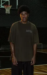 Remera de manga corta y cuello redondo, calce oversize, color marrón oscuro con efecto batik artesanal. Presenta un estampado frontal con la palabra "RAVERS" en tipografía universitaria con borde blanco.