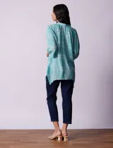 Blusa celeste con estampado de cachemir en blanco, cuello a la base, escote en V y abertura central con botones. Manga 3/4 regulable con presilla y botón, y terminación de ruedo asimétrico.