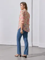Blusa de gasa estampada con flores en tonos rosa, amarillo y azul. Tiene cuello a la base con escote en V y botones. La parte delantera tiene detalle plisado y las mangas son 3/4 regulables con presilla y botón.