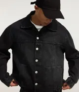 Campera masculina de jean negro con efecto desteñido, modelo boxy, con cuello solapa, manga larga con puño abotonado, cierre frontal con botones, bolsillos grandes y recortes.