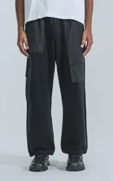Pantalón tipo jogger negro, de calce relajado, confeccionado en algodón y microfibra. Presenta paneles de microfibra en la parte superior y bolsillos cargo con fuelle en las piernas. Los tobillos son ajustables con cordón elástico.