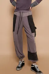 Pantalón babucha de tiro medio, color gris, con elástico en la cintura y cordón ajustable. Presenta bolsillos laterales y aplicaciones de tela en contraste simulando un diseño patchwork.