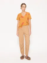 Remera color mostaza de punto flamé con estampado de labios rojos, escote en V profundo, mangas cortas y corte a la altura de la primera cadera.