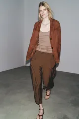 Pantalón cropped marrón de tiro medio y pierna ancha, confeccionado en hilatura con mezcla de lyocell. Presenta trabillas en la cintura, bolsillos laterales y pinzas en el delantero. Cierre frontal con cremallera y botón.