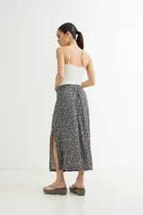 Falda midi fluida, color negro con estampado floral pequeño en blanco. Presenta un talle alto y una abertura lateral pronunciada.