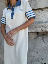 Vestido midi tejido en hilo color crema, con cuello polo azul y mangas cortas con rayas azules.