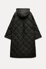 Chaqueta larga acolchada color negro con capucha y manga larga. Tiene bolsillos delanteros y bajo asimétrico con aberturas laterales. El cierre frontal es con botones ocultos por solapa.