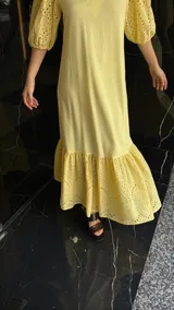 Vestido largo color amarillo pálido, con escote en V, mangas cortas abullonadas con detalle de calado y ruedo con volantes y calado.