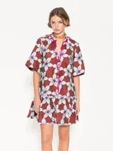 Vestido corto tipo túnica color ladrillo con estampado de flores celestes y violetas, cuello mao con lazo fucsia, mangas cortas y volado en el ruedo.