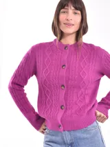 Cárdigan tejido color gris claro con diseño trenzado, cuello redondo y cierre frontal con botones marrones.