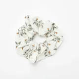Coletero de tela color blanco con estampado de hojas y flores pequeñas en tonos verdes y naranjas.