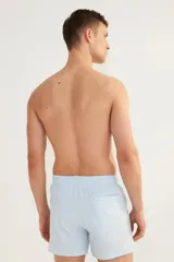 Short de baño celeste con rayas verticales blancas, de sirsaca, con aberturas laterales cortas, elástico en la cintura con cordón ajustable, bolsillos laterales y bolsillo trasero con cierre autoadherente. Suspensor interior de malla.