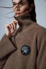 Sweater marrón de punto con cuello polo, cierre de cremallera parcial y parche bordado en el pecho.