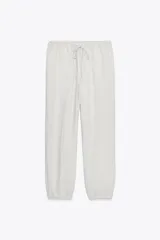 Pantalón jogger color gris claro, de tiro alto con cintura elástica ajustable con cordones, bolsillos delanteros y traseros con solapa, y puños elásticos en el bajo.