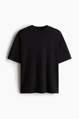 Remera negra de algodón de peso medio, con cuello redondo ribeteado, hombros caídos y bajo recto. Corte oversized para una silueta holgada.