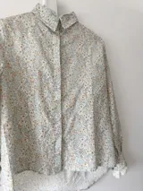 Camisa blanca estampada con flores pequeñas en tonos celeste, rosa y amarillo. Confeccionada en lino 100%, con botones de nácar y puntilla de algodón en los puños.