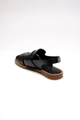 Sandalia negra de cuero con diseño tejido en el empeine, tira trasera con hebilla dorada ajustable y suela plana.