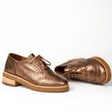 Zapato acordonado color bronce de cuero vacuno con perforaciones decorativas, taco de madera con folia en cuero de 4cm y entre suela de goma de 1,5cm. Horma de punta redonda y cómoda.