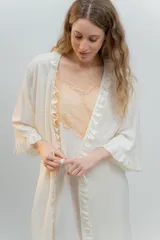 Bata kimono gris claro de algodón con volados en mangas y ruedo. Tiene mangas al codo y lazo de algodón para ajustar en la cintura.