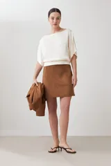 Blusa color beige, de tela satinada, con mangas cortas y cuello redondo.