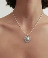 Collar plateado con cadena de eslabones y dije en forma de corazón con detalles ornamentales y una piedra en el centro.