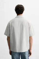 Camisa de manga corta con cuello bowling y corte relaxed fit, confeccionada en tejido con algodón y diseño a rayas verticales en tonos beige y blanco.