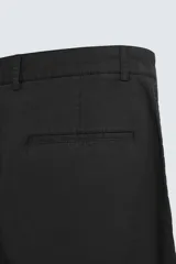 Pantalón negro de corte recto confeccionado en tejido de algodón con elasticidad. Presenta pliegues en la parte delantera, bolsillos laterales y traseros de vivo. Cierre frontal con cremallera y botón.