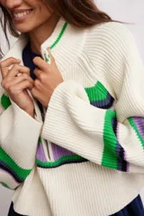 Sweater de punto color crudo con rayas horizontales verdes, violetas y negras, de cuello alto con cierre parcial y mangas largas acampanadas.