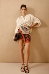 Pareo de algodón con estampado floral en tonos beige, negro y naranja. Detalle de borlas en el ruedo.