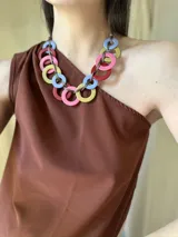 Collar con aros de acrílico entrelazados con tiento sintético color chocolate. Tiene nudo ajustable para regular el largo.