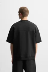 Sudadera negra de corte relaxed fit, confeccionada en tejido interlock de algodón con elasticidad. Tiene cuello redondo, manga corta y bajo acabado en rib.