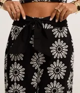 Pantalón zanahoria de cintura alta, confeccionado en laise negro con bordado floral blanco y lazo en la cintura.