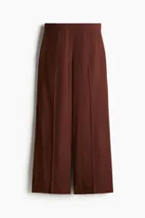 Pantalón ancho color marrón chocolate, de tiro alto con elástico en la parte posterior de la cintura y cierre oculto con corchete en un lado. Presenta bolsillos laterales discretos y piernas amplias con pliegues adelante y atrás.