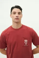 Remera celeste de manga corta con bolsillo en el pecho y estampado con palmera y texto.