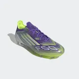 Championes de fútbol Adidas F50 Elite para terreno firme, con exterior en tonos morado iridiscente y verde lima, tres franjas plateadas y cordones morados. Poseen suela con tapones transparentes.